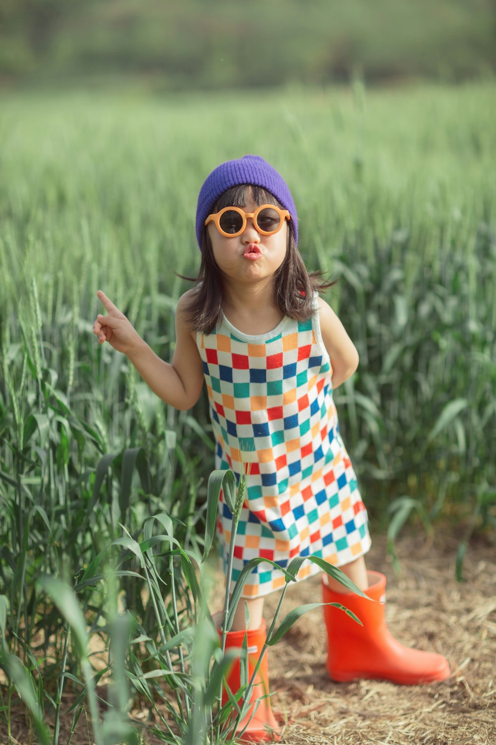 a little girl wearing sunglasses and a hat standing in a field