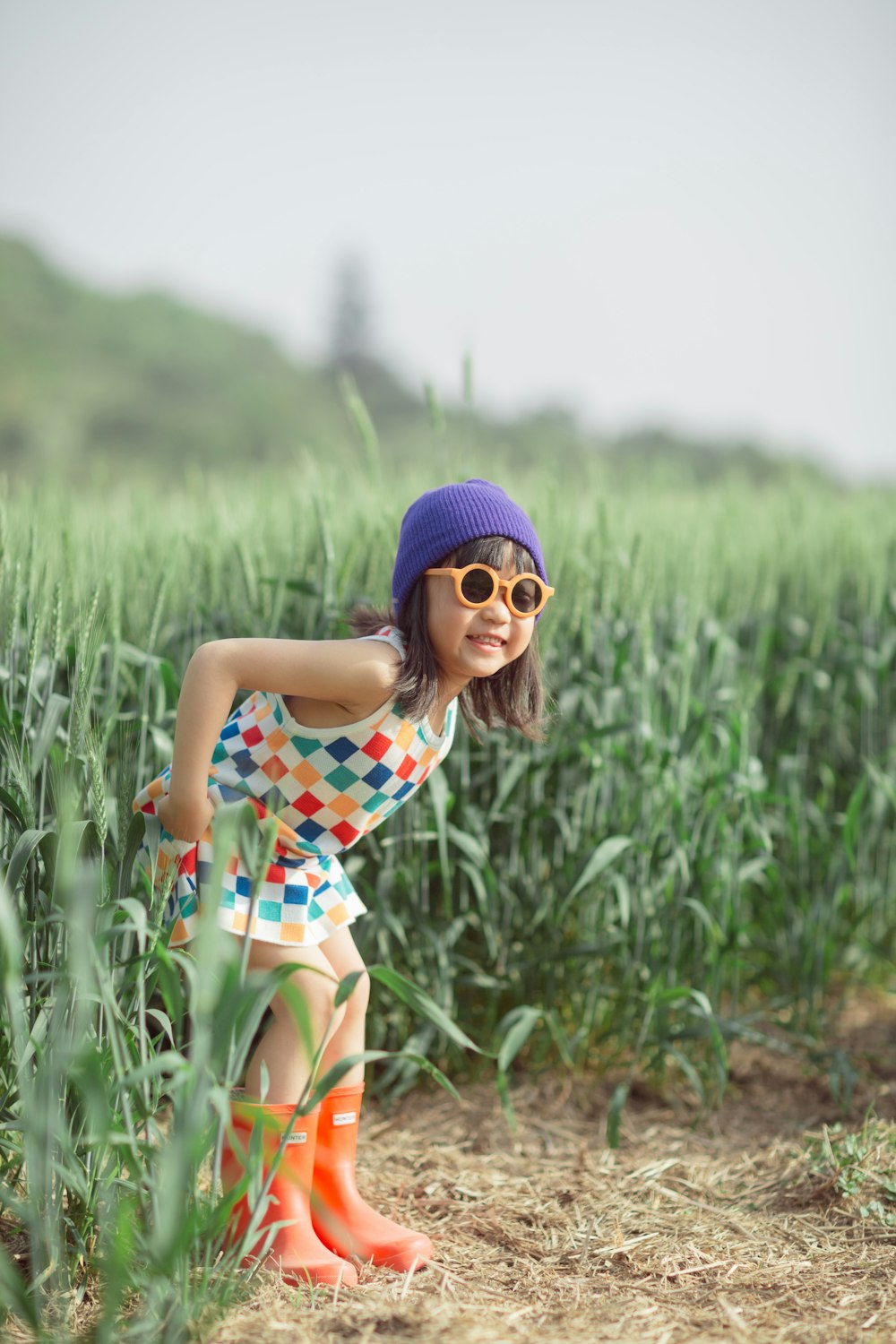 a little girl in a colorful dress and rain boots in a field