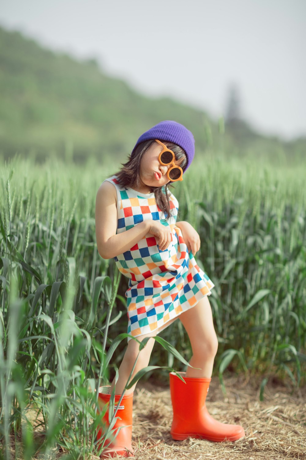 a little girl in a colorful dress and hat standing in a field