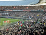 A crowded football stadium filled with enthusiastic fans. Many are holding colorful inflatable beach balls and other objects. The vibrant scene is set against a clear view of the pitch and goalposts. Banners and signs for the UEFA Europa League are prominently displayed, creating a lively and festive atmosphere.
