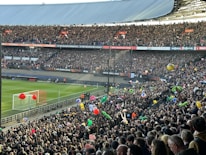 A crowded football stadium filled with enthusiastic fans. Many are holding colorful inflatable beach balls and other objects. The vibrant scene is set against a clear view of the pitch and goalposts. Banners and signs for the UEFA Europa League are prominently displayed, creating a lively and festive atmosphere.