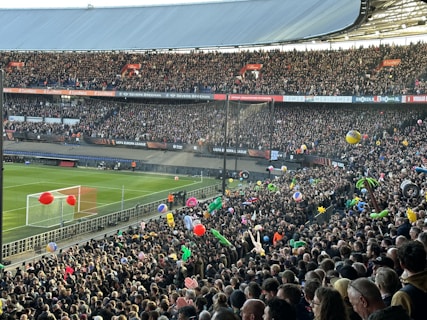 A crowded football stadium filled with enthusiastic fans. Many are holding colorful inflatable beach balls and other objects. The vibrant scene is set against a clear view of the pitch and goalposts. Banners and signs for the UEFA Europa League are prominently displayed, creating a lively and festive atmosphere.