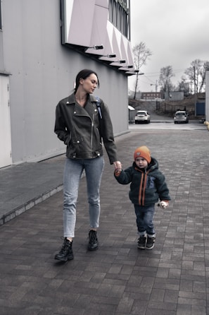 A mother and child wearing oversized denim jackets, walking through a golden maple leaf-lined street.