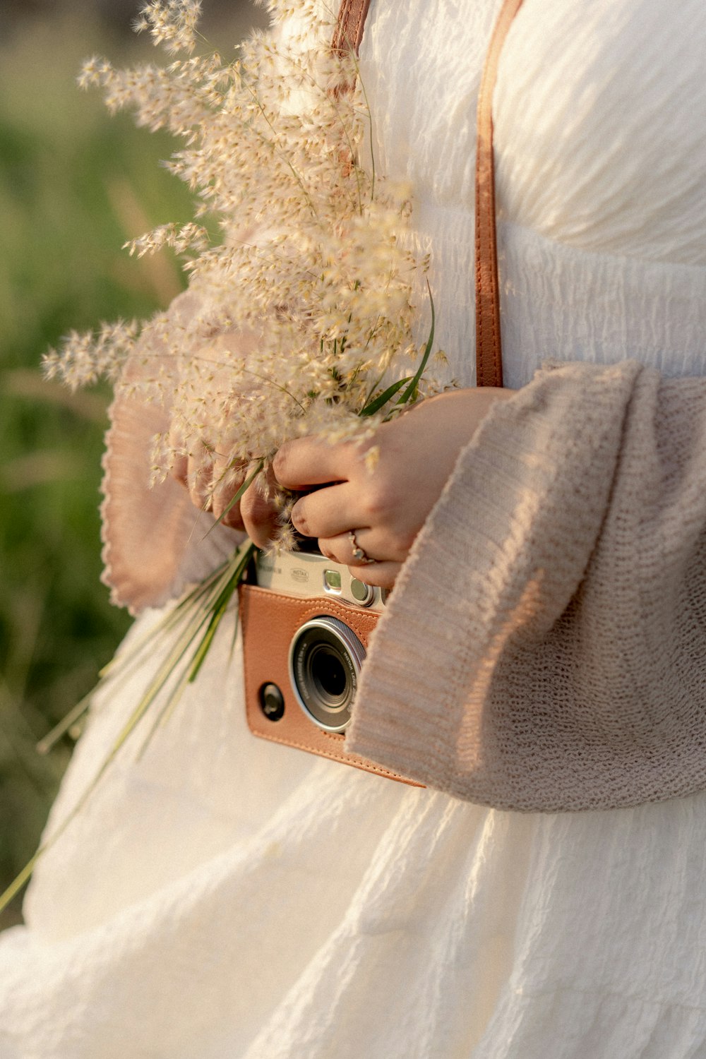 Eine Frau in einem weißen Kleid, die eine Kamera und Blumen hält