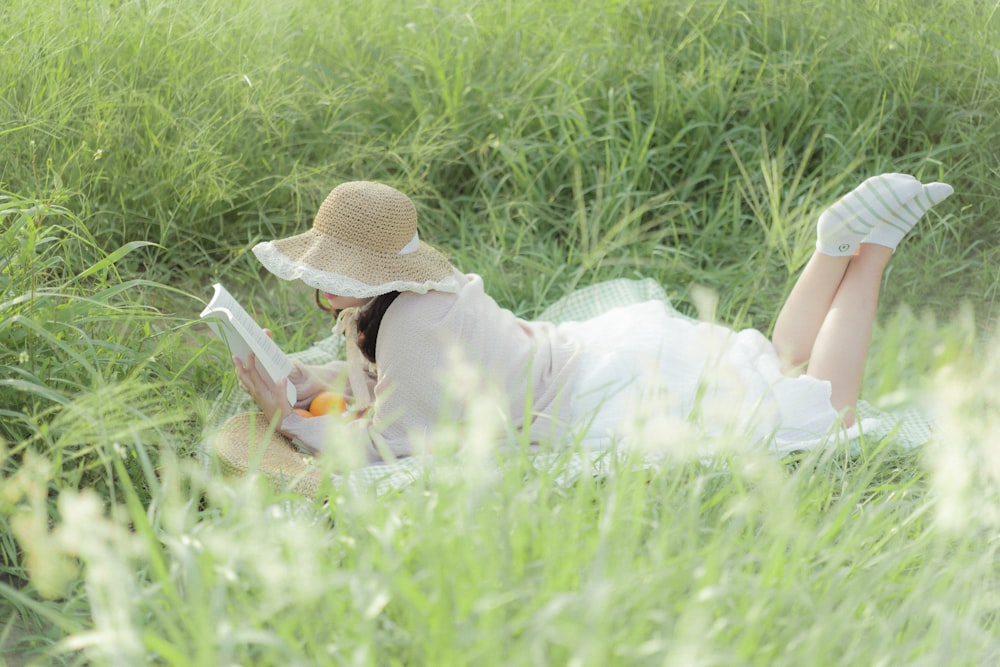 a woman laying in the grass reading a book