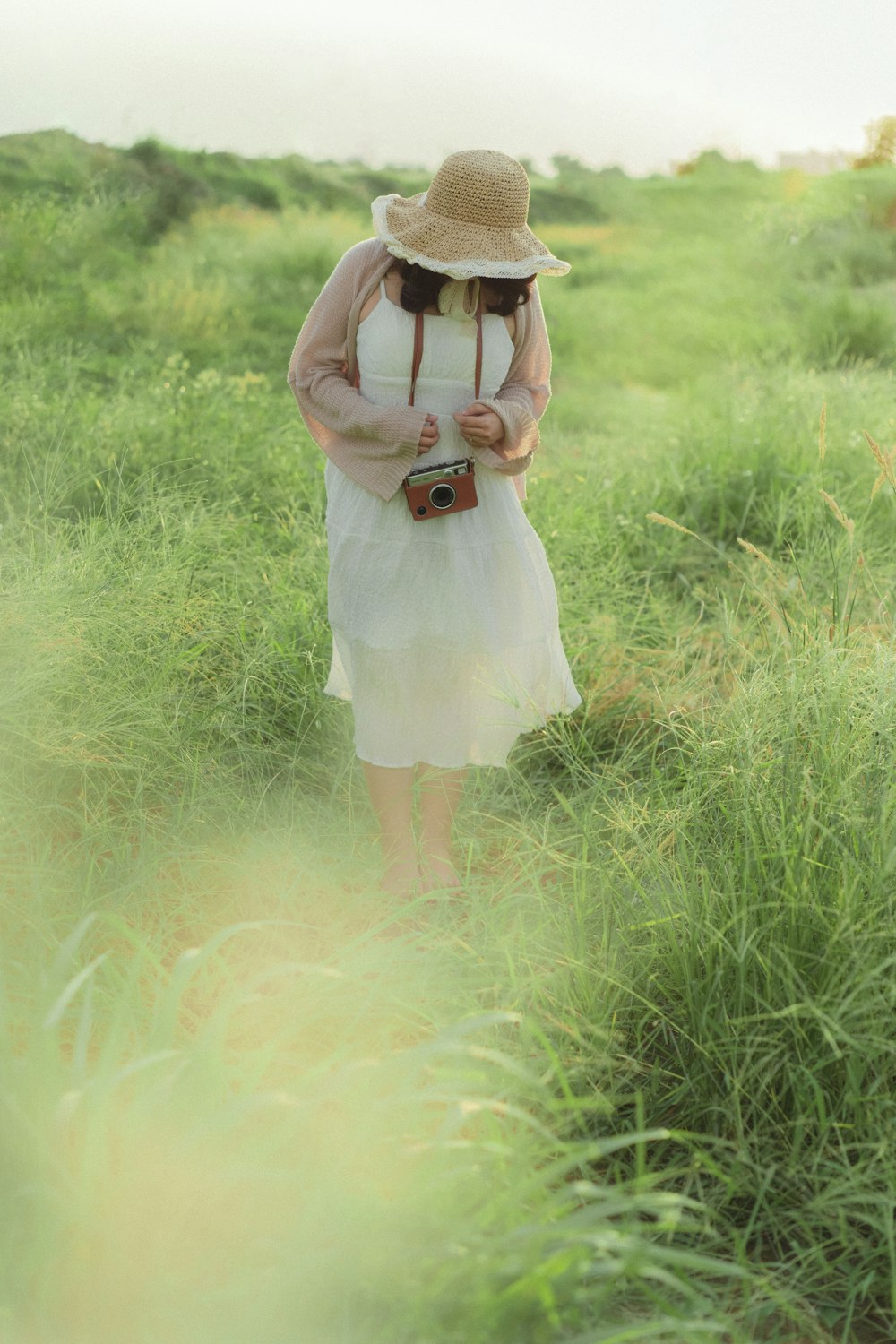 a woman in a white dress and hat walking through tall grass