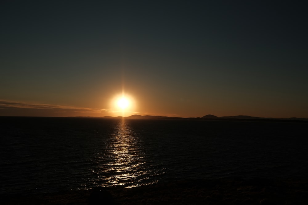 the sun is setting over the ocean with mountains in the background