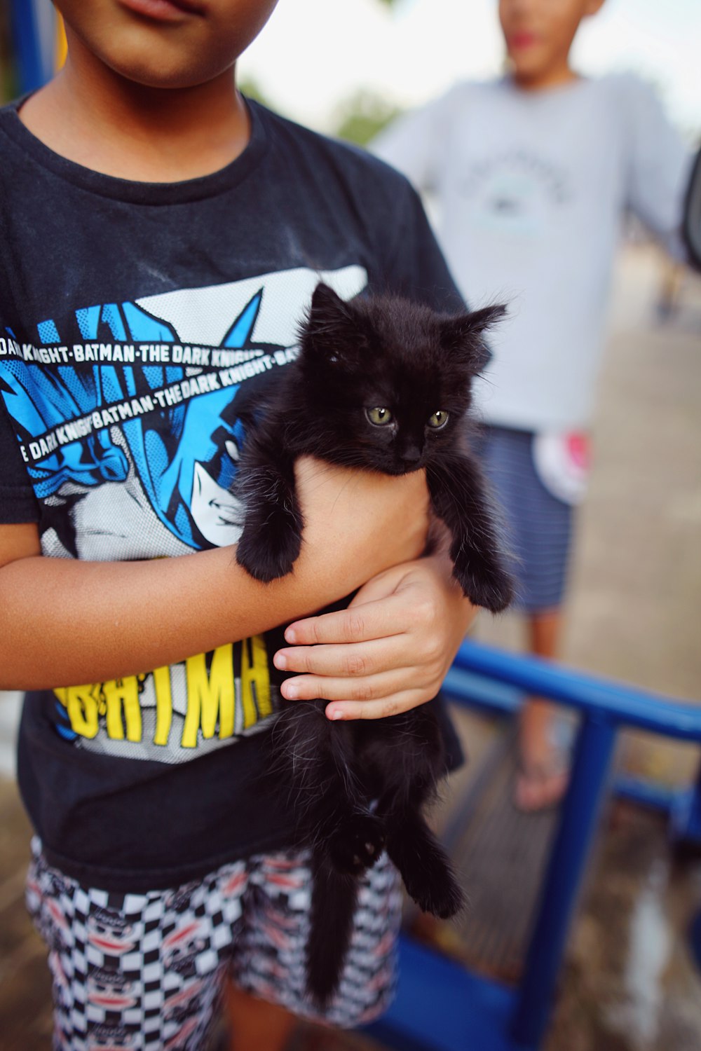 a young boy holding a black kitten in his arms