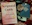 A book titled '7 Mental Ailments' lies next to a pair of black-rimmed glasses, a large beige flower, and another book titled 'The Bible Promise Book.' These items are placed on a textured, multicolored knitted fabric, and there is a black cup next to the items.