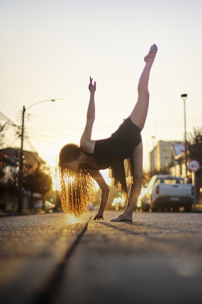 Dancer performing expressive movement on an urban street at sunset.