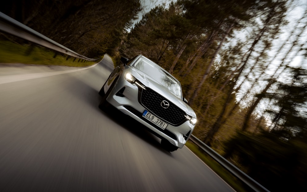 a white car driving down a road next to a forest