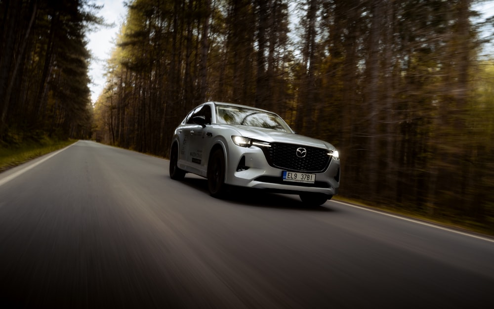 a silver car driving down a road next to a forest