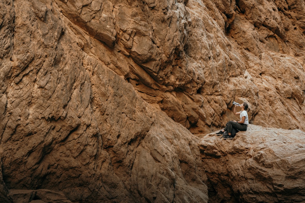 uma mulher sentada no topo de uma rocha ao lado de um penhasco
