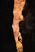 Climber scaling a steep cliff face with dramatic shadows and textured rock.
