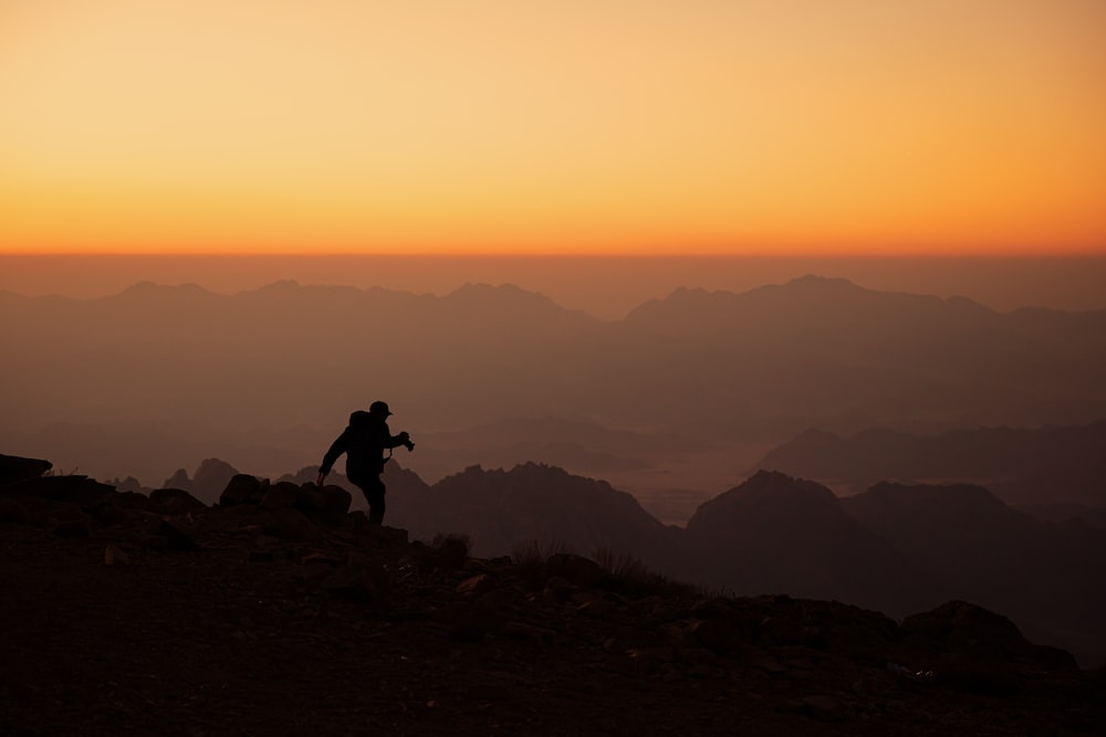 eine Person, die bei Sonnenuntergang auf dem Gipfel eines Berges steht