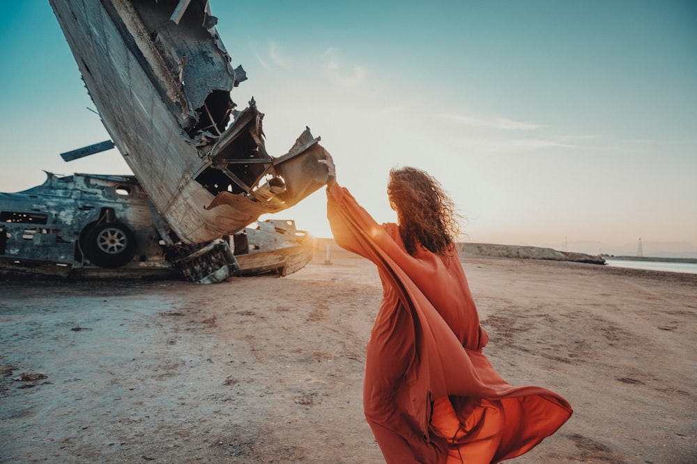 uma mulher com um vestido laranja em frente a um avião destruído