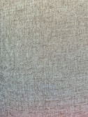 A close-up view of a textured fabric with a woven pattern. The fabric appears to be coarse with visible individual threads creating a consistent, grid-like design.
