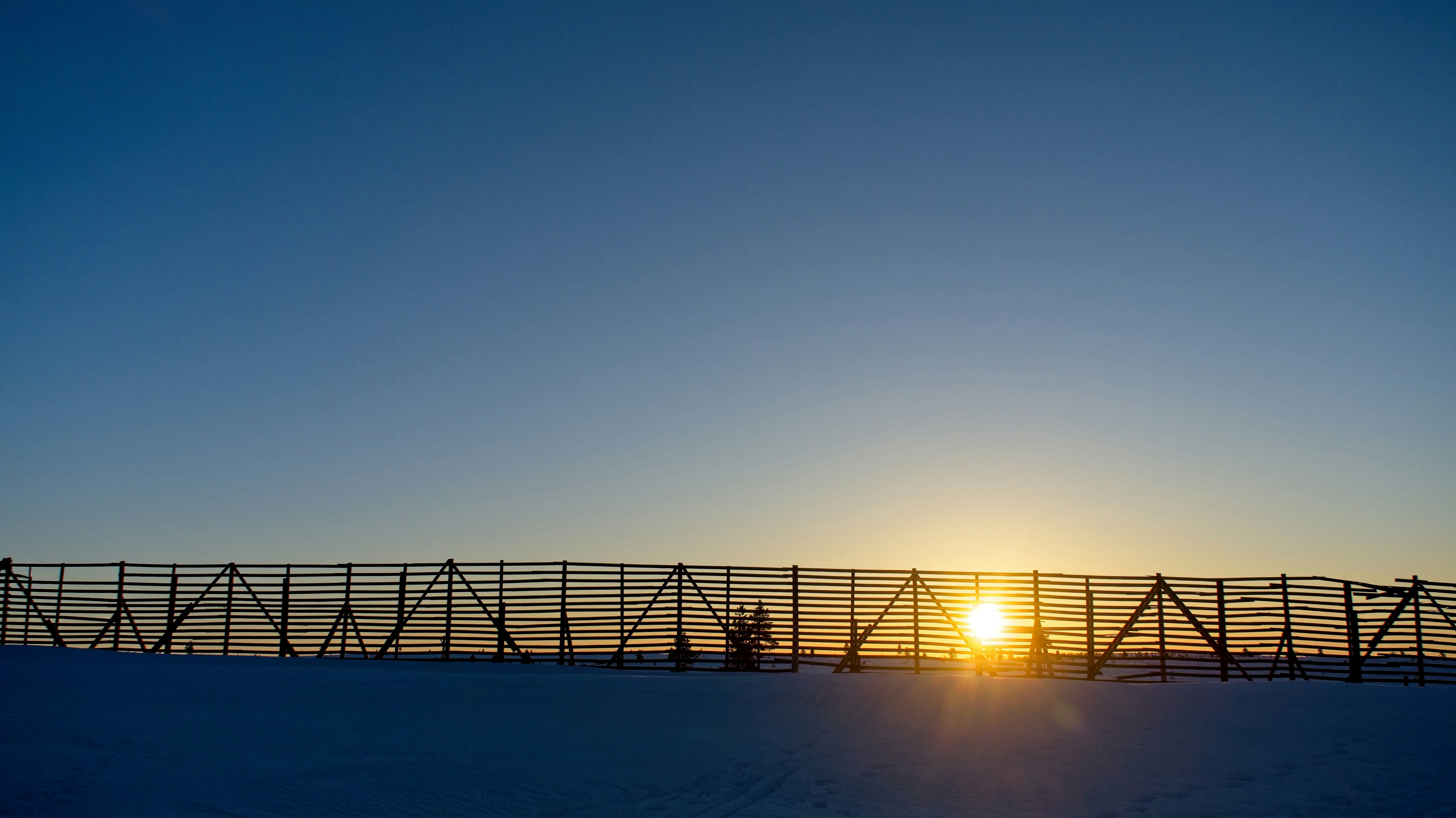 the sun is setting behind a fence in the snow