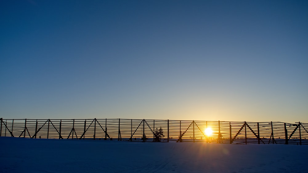 the sun is setting behind a fence in the snow