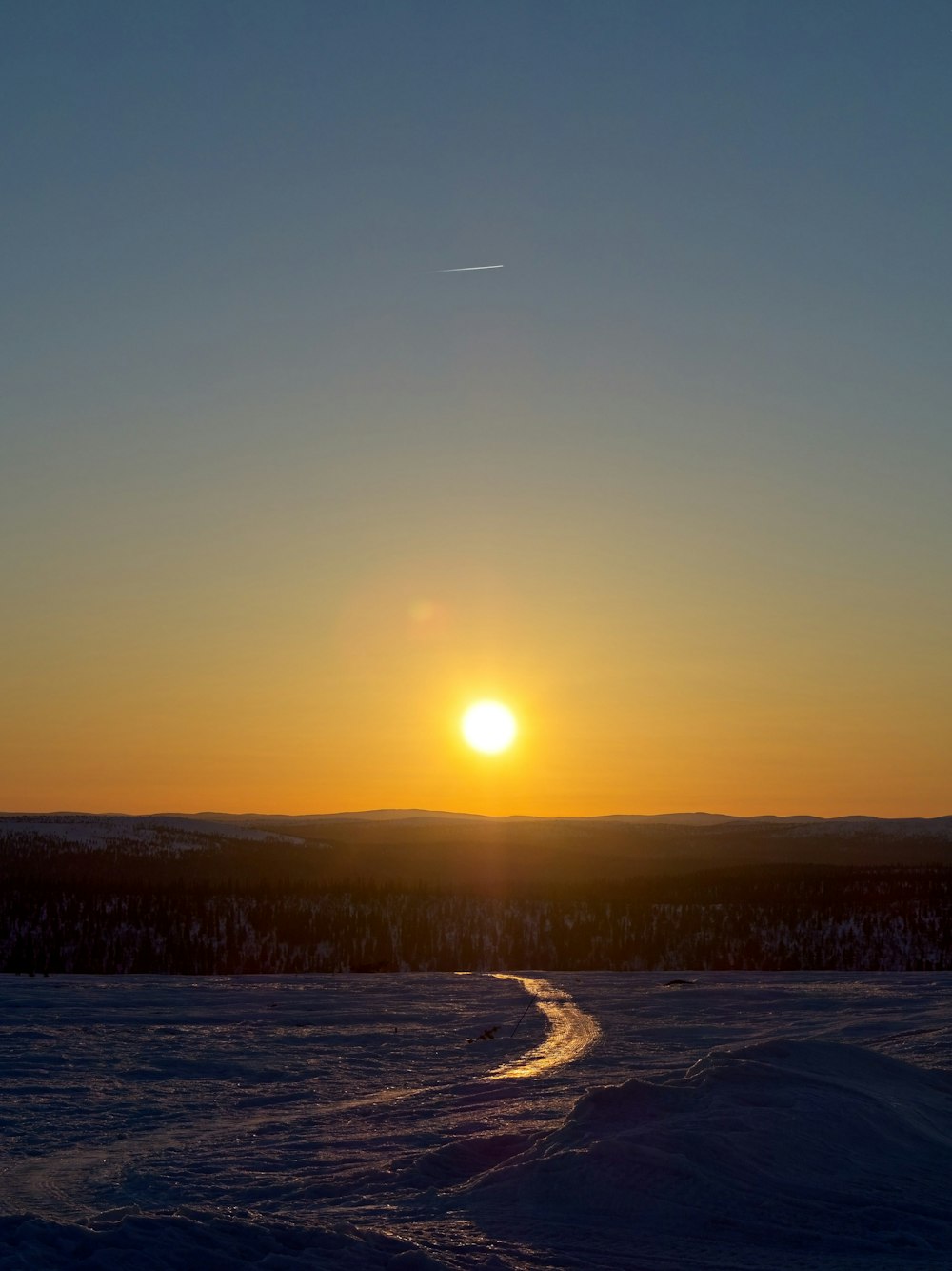 the sun is setting over a snowy field