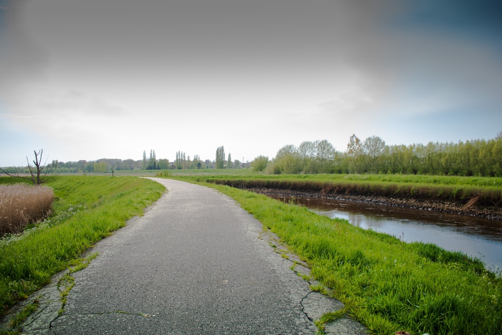 a paved path next to a river in a green field
