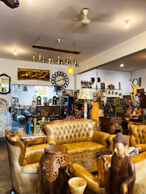An antique shop filled with vintage furniture and decor. Leather sofas and ornate wooden tables dominate the space. The ceiling hosts a series of small pendant lights. The room is accessorized with different decorative items, including mirrors, artwork, and sculptures.