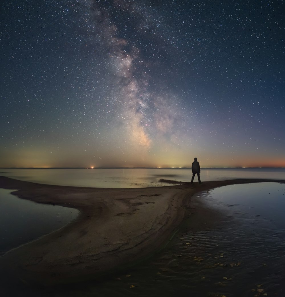 a man standing on a beach under a night sky