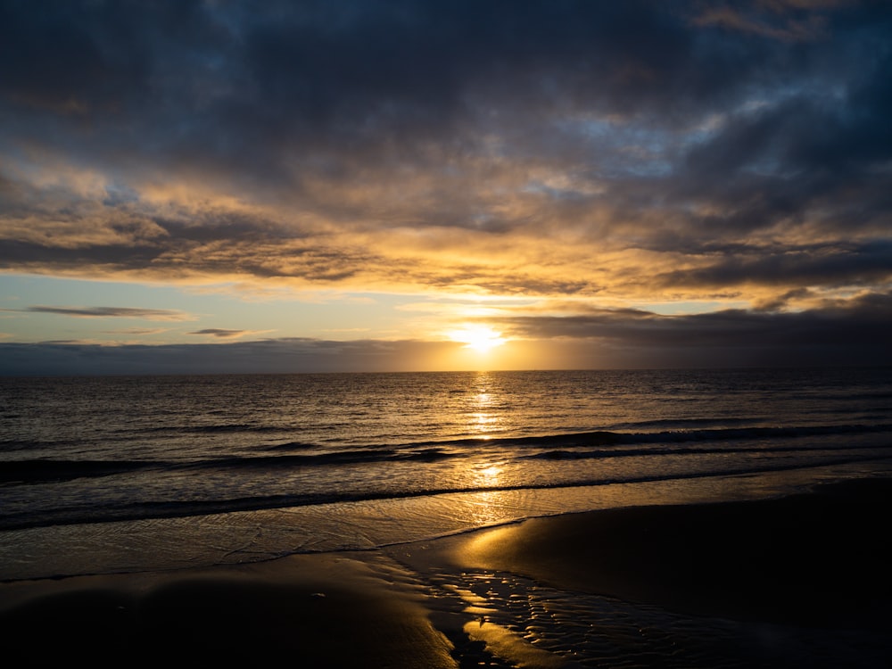 the sun is setting over the ocean on a cloudy day