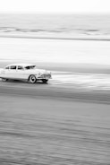 A black and white shot of a vintage Puma speeding on a coastal road.