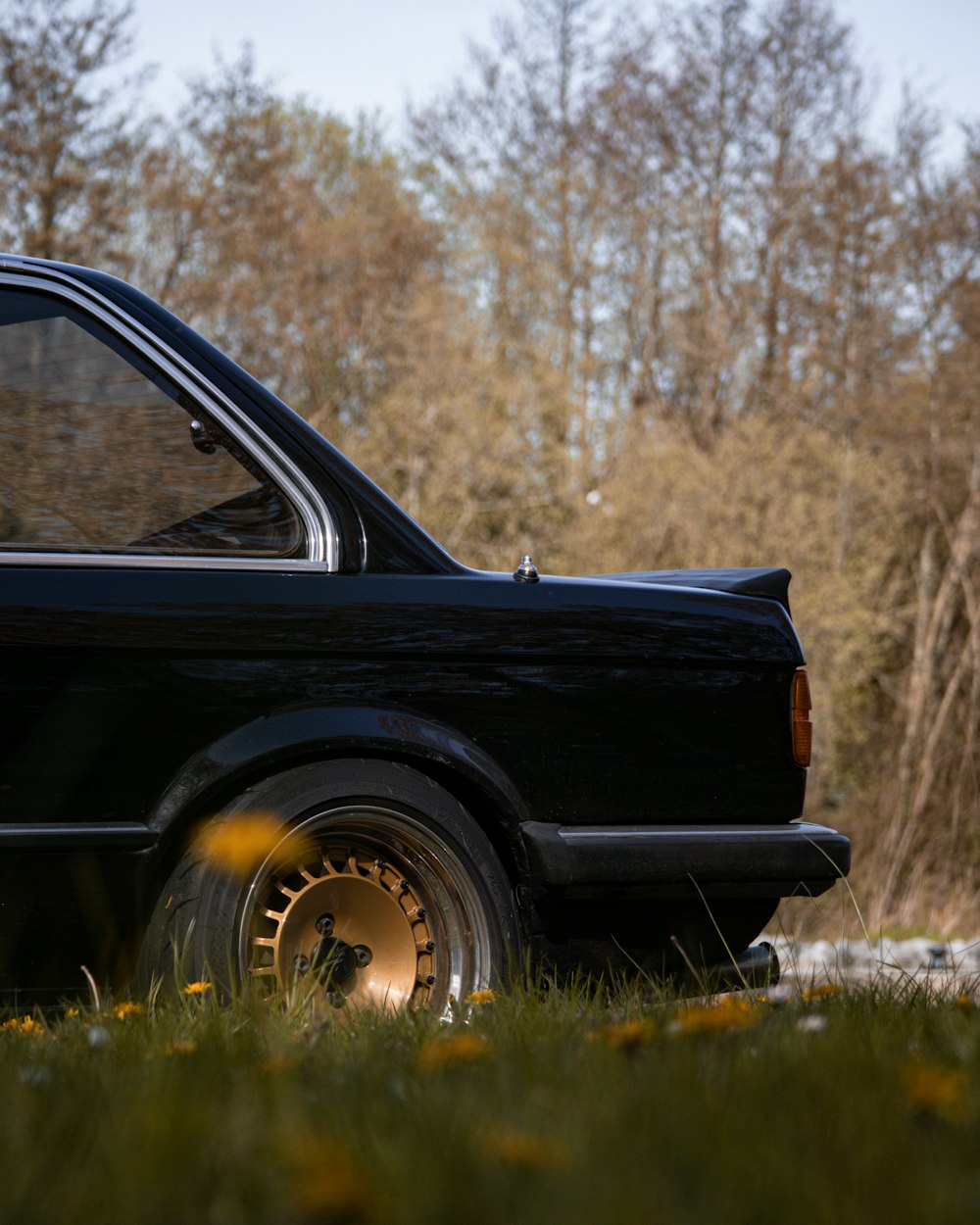 a black car parked in a field with trees in the background