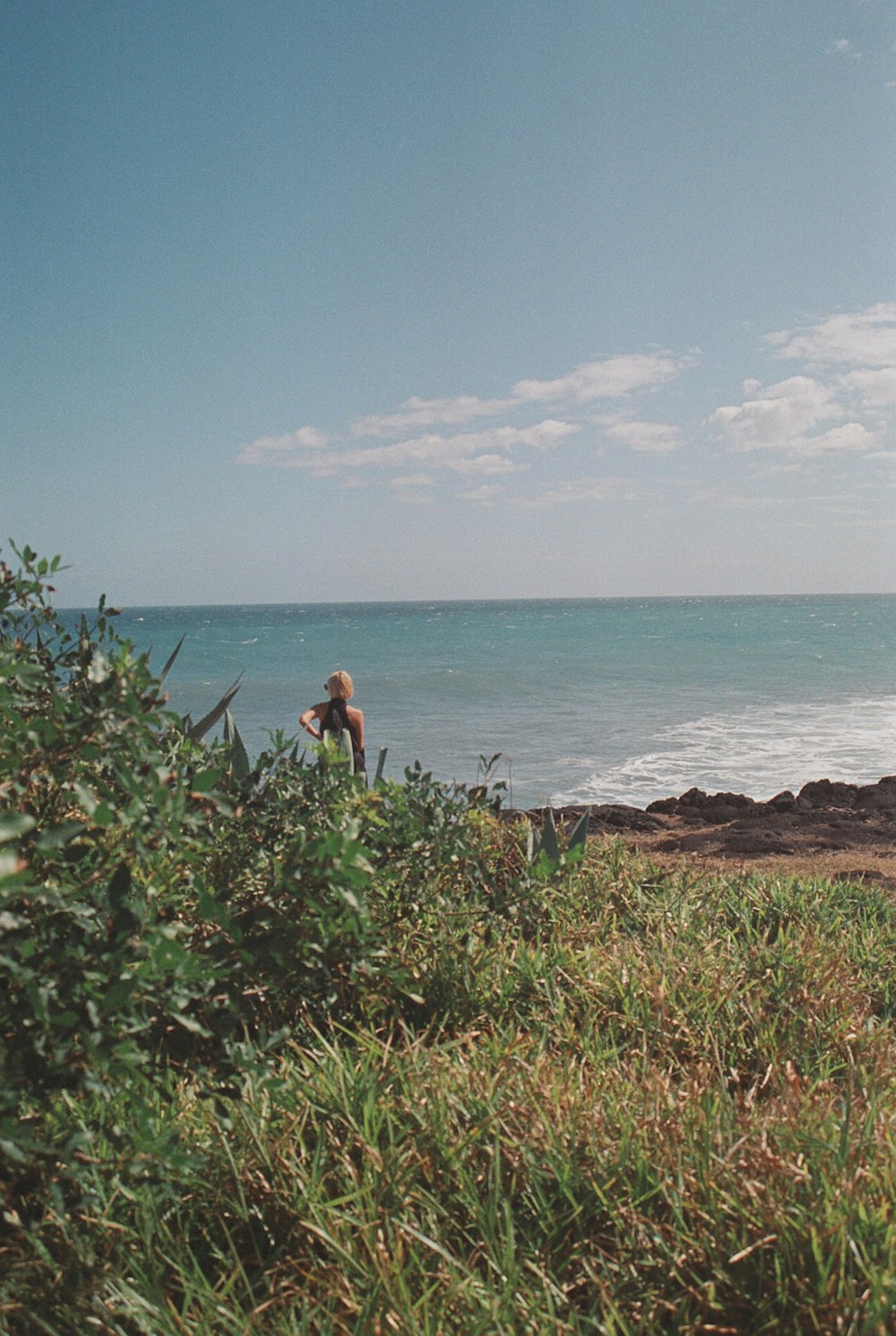 a man standing on top of a lush green hillside next to the ocean