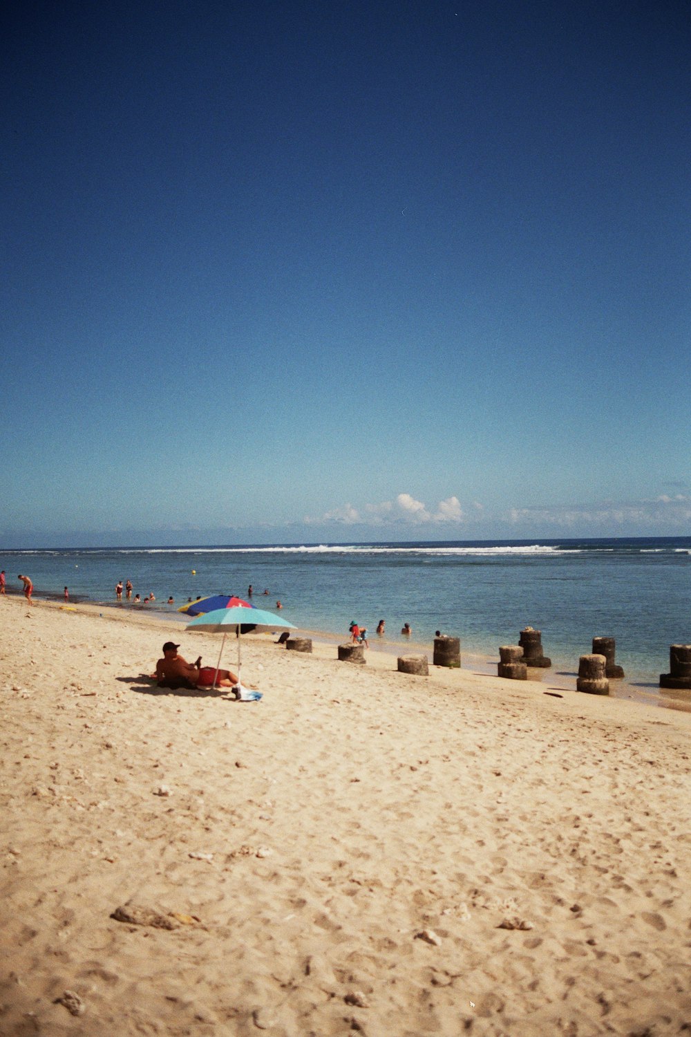 a sandy beach with a blue umbrella and people in the water