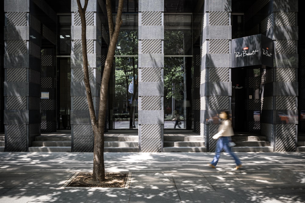 a woman walking down a sidewalk past a tall building