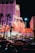 A brightly lit casino with neon lights in vibrant red, pink, and blue, featuring a large flamingo signage. Palm trees are visible in the foreground with vehicles passing by on the street at night.