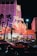 A brightly lit casino with neon lights in vibrant red, pink, and blue, featuring a large flamingo signage. Palm trees are visible in the foreground with vehicles passing by on the street at night.