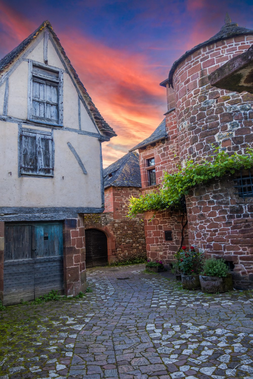 a cobblestone street leading to a building with a red sky in the background