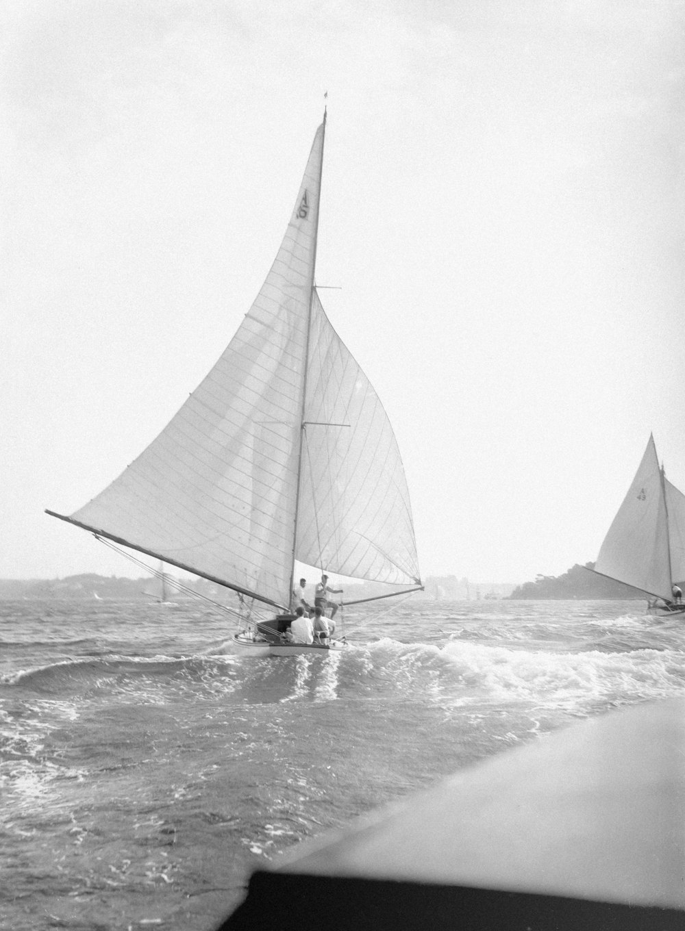 a black and white photo of two sailboats in the ocean