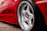Close-up photo of a shiny black and silver car rim installed on a sleek red car.