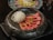 A beautifully presented dish featuring slices of seared tuna garnished with herbs, arranged alongside a portion of thinly sliced white radish. The food is placed in a textured black bowl, with another dish visible in the background blurred out.