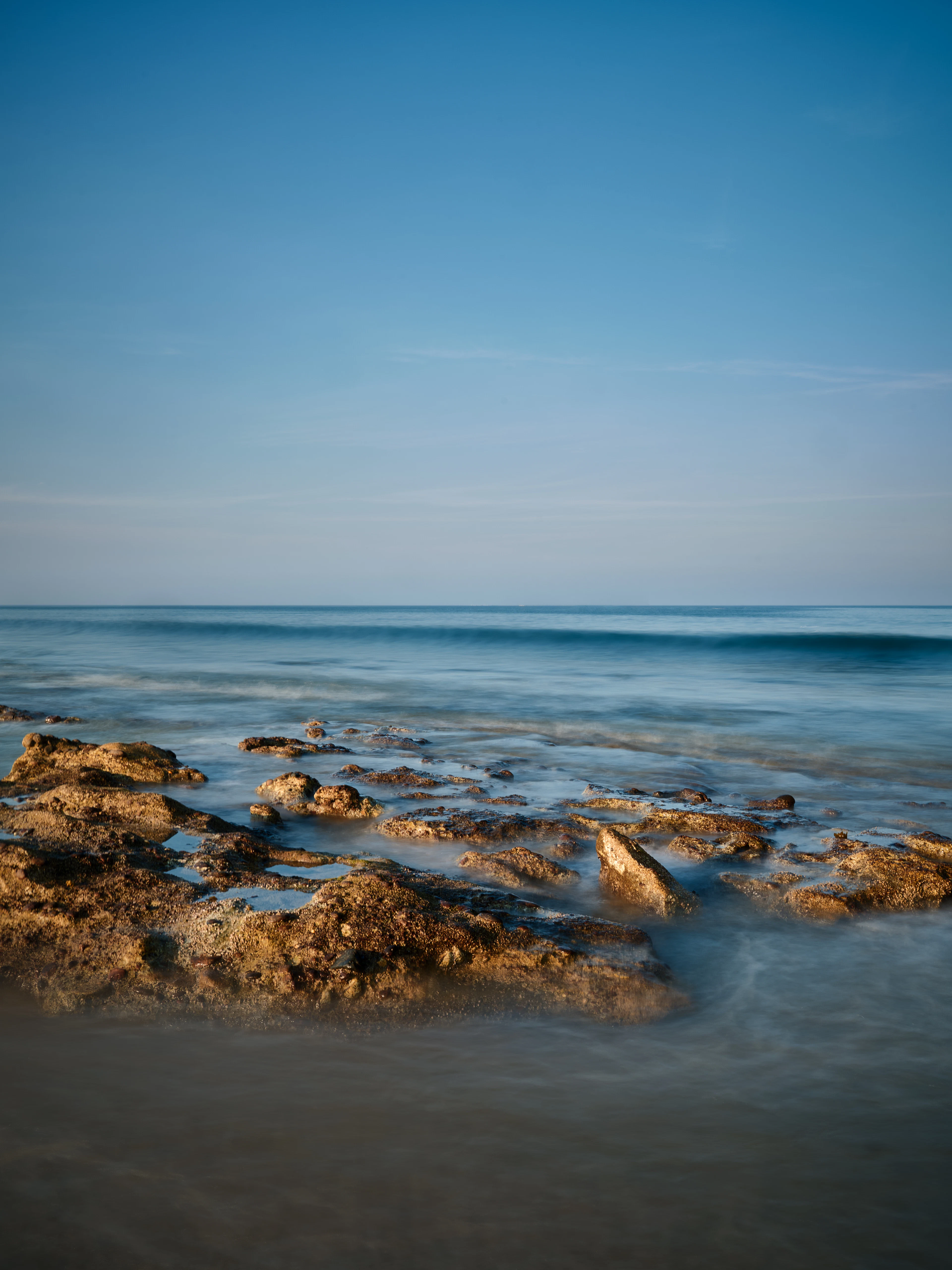 A rocky shore and gentle waves in evening light on the coast at Dibba, Fujairah
