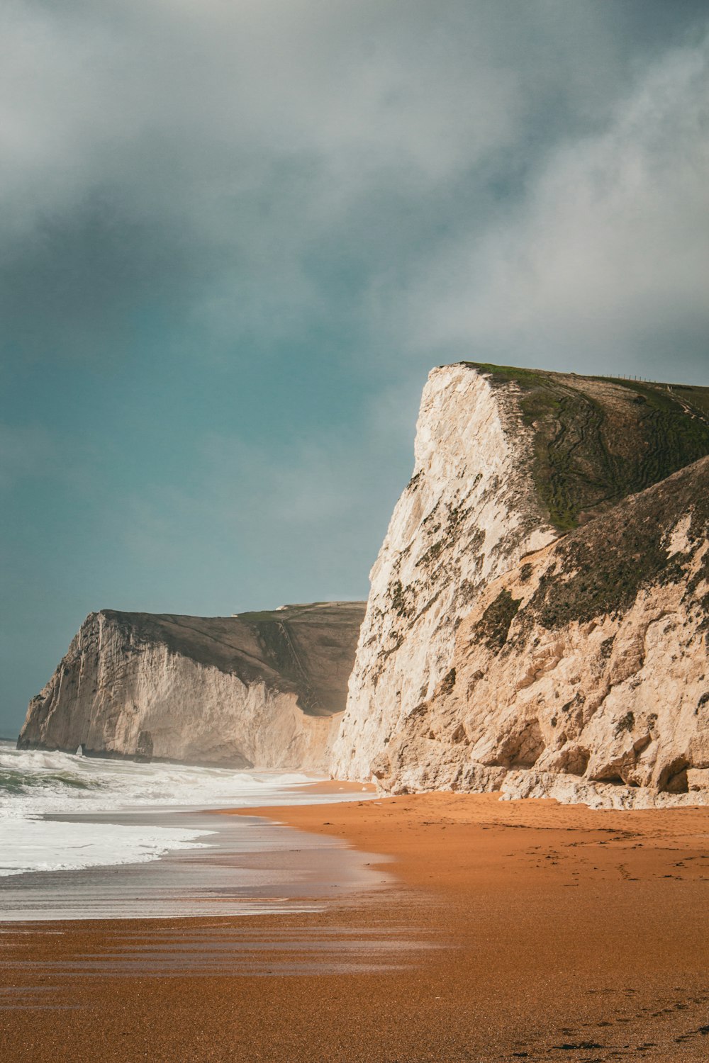 a sandy beach next to a large white cliff