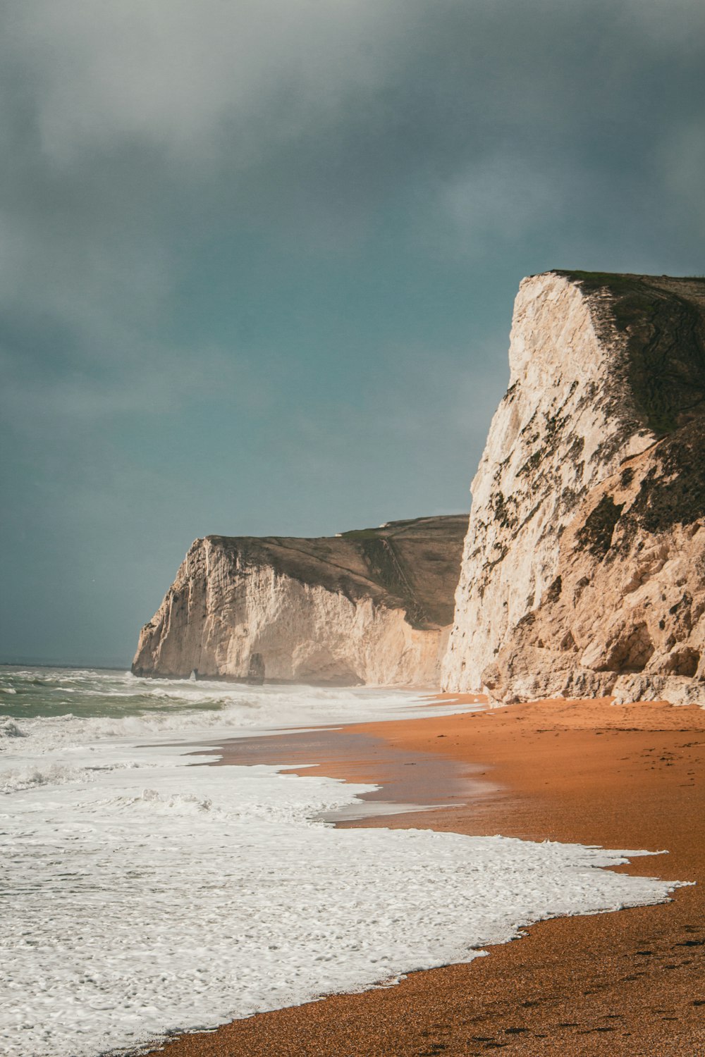 a person walking on a beach next to a cliff