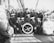 A group of sailors wearing uniforms and caps are gathered on the deck of a ship. The men are arranged in a casual pose around a large life ring. The ship’s deck is equipped with nautical gear such as ropes and machinery, visible in the background and to the sides.