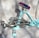 A turquoise exercise machine with metallic handles and a padded seat in contrasting colors. The design appears sturdy with a combination of steel and cushioned parts, designed for workouts. The background is a neutral fabric backdrop, providing a simple yet effective contrast to the machine.