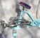 A turquoise exercise machine with metallic handles and a padded seat in contrasting colors. The design appears sturdy with a combination of steel and cushioned parts, designed for workouts. The background is a neutral fabric backdrop, providing a simple yet effective contrast to the machine.