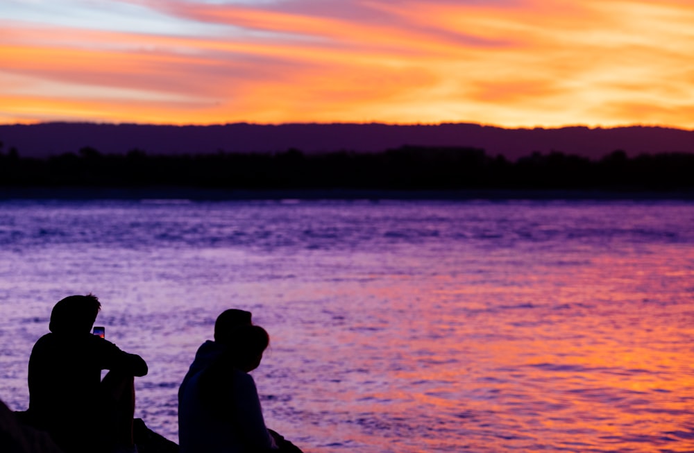 Dos personas sentadas en un muelle viendo la puesta de sol