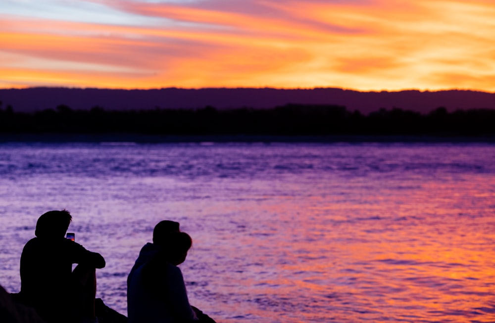 Deux personnes assises sur un quai regardant le coucher du soleil