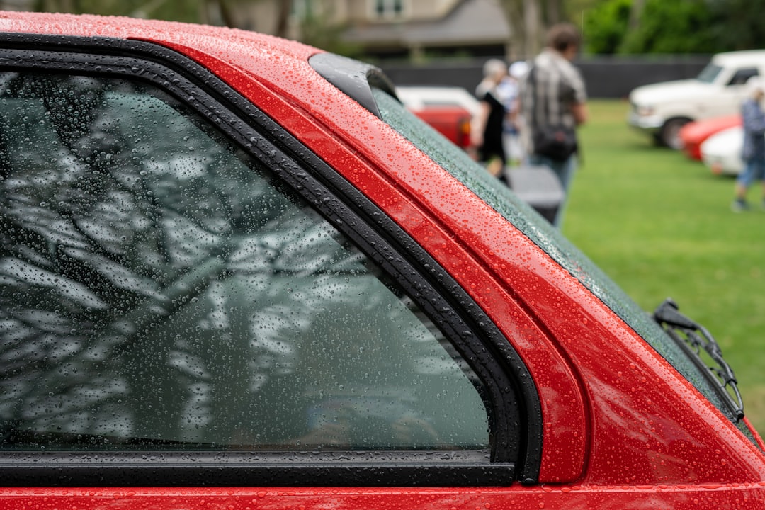 a red car parked in a parking lot next to a lush green field,
