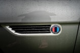 Raindrops cover the metallic surface of a vehicle, focusing on an emblem that reads 'Smit Vehicle Engineering' with a multicolored design. The background is slightly blurred, highlighting the text and colors.
