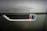 Raindrops cover the metallic surface of a vehicle, focusing on an emblem that reads 'Smit Vehicle Engineering' with a multicolored design. The background is slightly blurred, highlighting the text and colors.